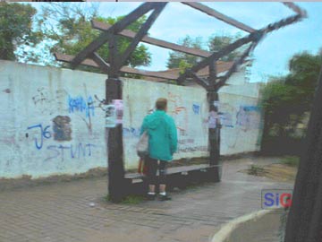 Sin techo: una señora espera el colectivo bajo la lluvia, en paseo 107